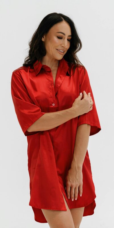 Elegant woman in a silky red dress poses fashionably with a confident smile.