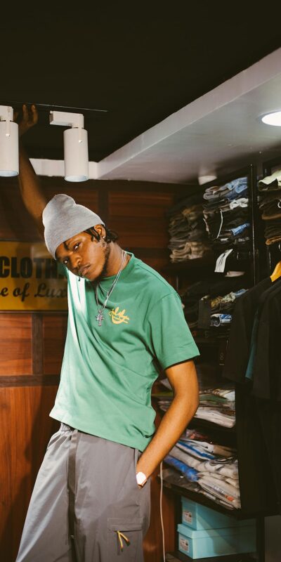 Man posing stylishly in a fashion store wearing a green t-shirt and beanie.