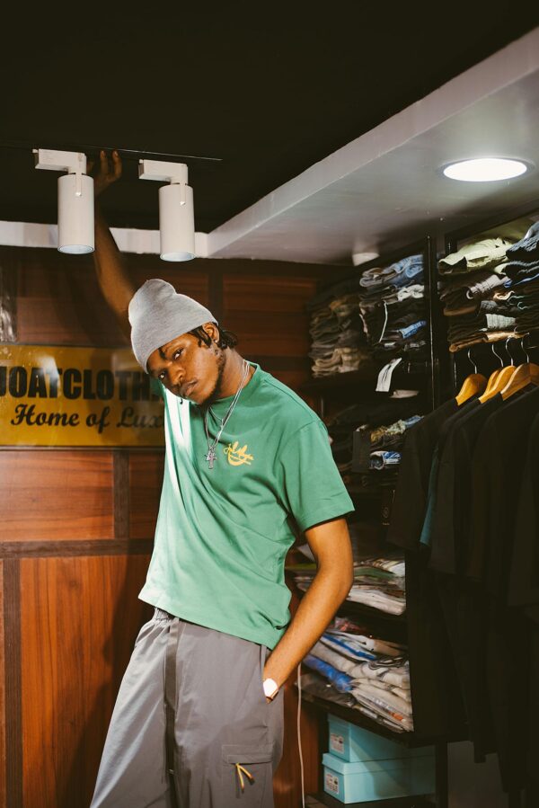 Man posing stylishly in a fashion store wearing a green t-shirt and beanie.