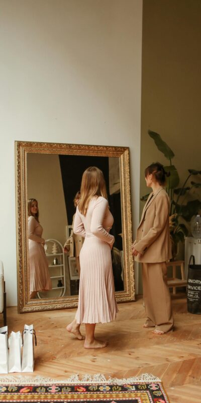 Two women shopping and trying on clothes indoors with a large ornate mirror.